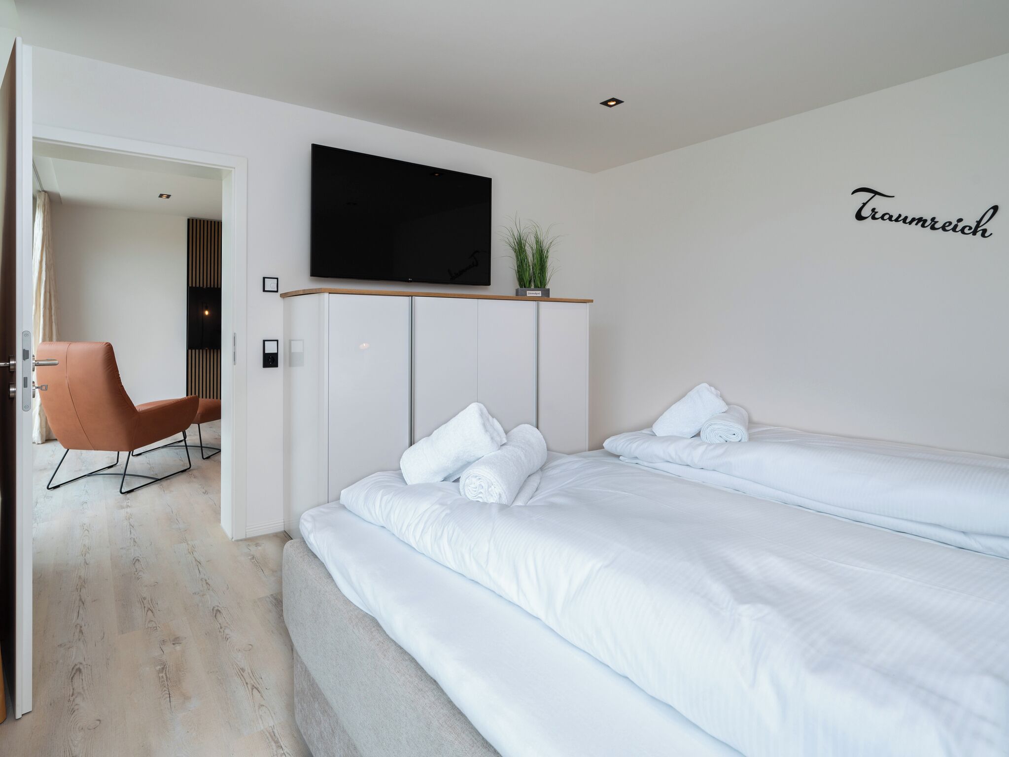 Een moderne hotelkamer met een bed, een aan de muur bevestigde televisie, een stoel en een bord met de naam 'Traumreich'.