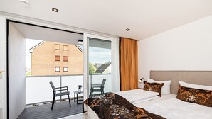 Habitació d'hotel moderna amb un llit gran, un balcó amb dues cadires i vista a un edifici de maó.