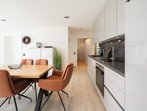 A modern kitchen with white cabinets, a black countertop, and stainless steel appliances. There is a dining area with a wooden table and leather chairs. - Inseltörn apartment 8<br>Large apartment in a prime location and access to the sea time (Büsum)