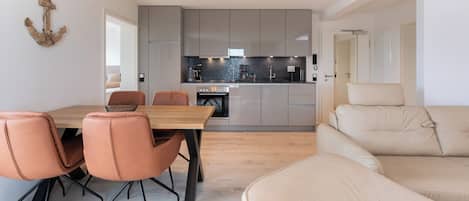 A modern kitchen with grey cabinets, a wooden dining table, and orange chairs.