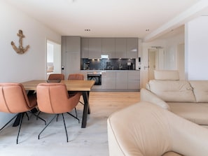 Une cuisine moderne avec des meubles de couleur grise, une table à manger en bois et des chaises orange.