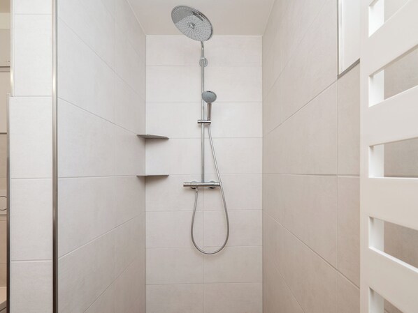 En moderne bruseniche med både håndbruser og brusehoved i loftet, monteret på en væg med et enkelt design.
