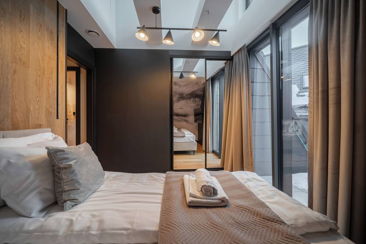 A modern hotel room with a large bed, a view through a glass door, and a ceiling light fixture.