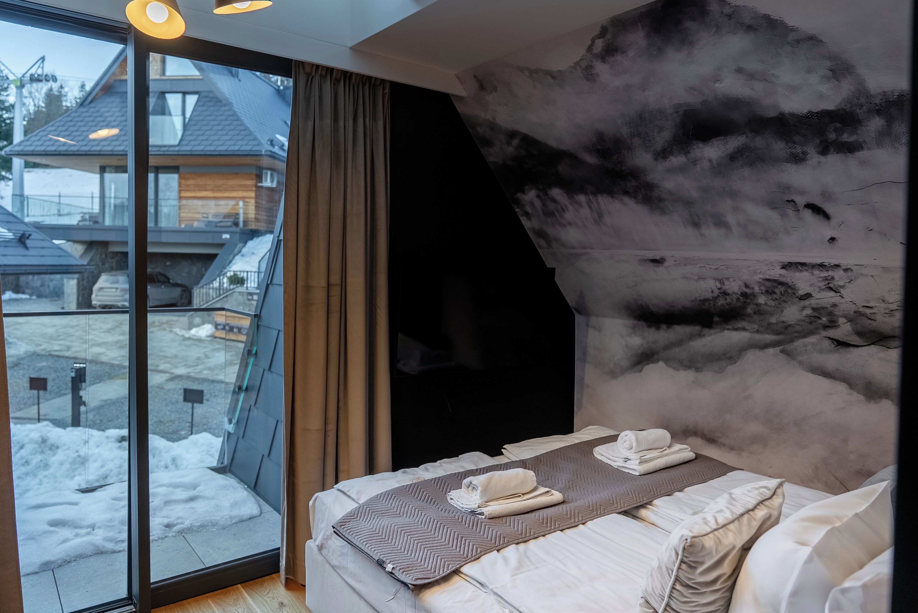 Une chambre d’hôtel moderne dotée d’une grande fenêtre, d’un lit avec des serviettes soigneusement pliées et d’un mur décoratif original en pierre.