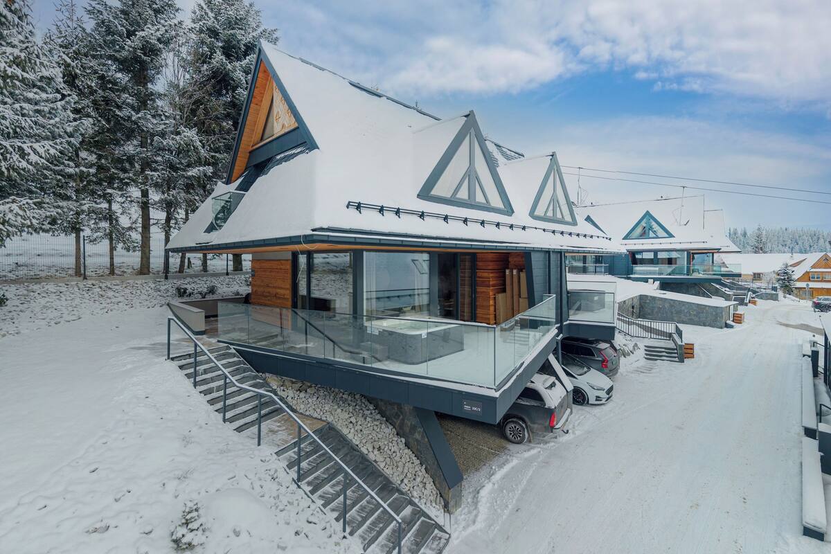 A modern cabin with a glass balcony, a wooden deck, and a ski lift in the background.