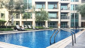 A swimming pool with lounge chairs and a building with multiple balconies in the background. - Stayshort - Luxury 2 Bedroom in Downtown That Sleeps 4 With Balcony (Dubai)