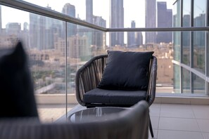 A balcony with a wicker chair and a glass table, overlooking a cityscape with tall buildings. - Stayshort - Luxury 2 Bedroom in Downtown That Sleeps 4 With Balcony (Dubai)