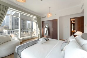 A modern hotel room with a large bed, a sofa, a balcony with a city view, and a wardrobe. - Stayshort - Luxury 2 Bedroom in Downtown That Sleeps 4 With Balcony (Dubai)