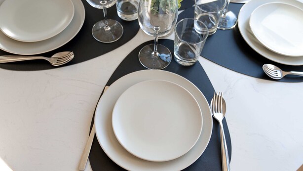A table set with plates, cutlery, and glasses, arranged on a white table with a black placemat. - Stayshort - Luxury 2 Bedroom in Downtown That Sleeps 4 With Balcony (Dubai)