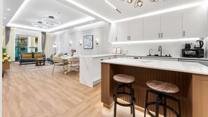 A modern kitchen with white cabinets, a marble countertop, and a wooden island with stools. - Stayshort - High-floor 1 Bedroom in Dubai Marina That Sleeps 2 (Dubai)