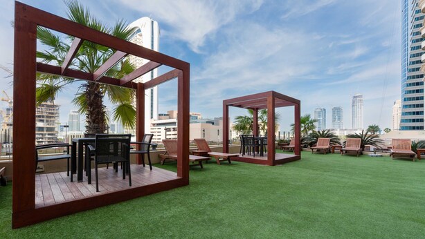A rooftop garden with wooden pergolas, seating areas, and artificial grass. - Stayshort - High-floor 1 Bedroom in Dubai Marina That Sleeps 2 (Dubai)