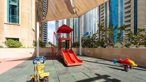 A playground with a slide and swings in an urban setting with tall buildings in the background. - Stayshort - High-floor 1 Bedroom in Dubai Marina That Sleeps 2 (Dubai)