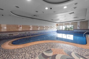 An indoor swimming pool with a tiled floor and walls, a curved design, and a window providing natural light. - Stayshort - High-floor 1 Bedroom in Dubai Marina That Sleeps 2 (Dubai)