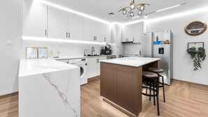 A modern kitchen with white cabinets, a marble island, a built-in washing machine, and a refrigerator with a water dispenser. - Stayshort - High-floor 1 Bedroom in Dubai Marina That Sleeps 2 (Dubai)