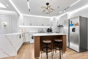 A modern kitchen with white cabinets, a central island with stools, a stainless steel refrigerator, and a built-in washing machine. - Stayshort - High-floor 1 Bedroom in Dubai Marina That Sleeps 2 (Dubai)