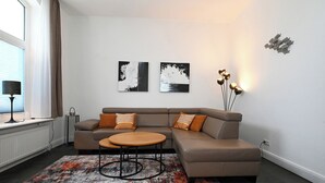 Un salon moderne avec un canapé d’angle, une table basse ronde, des œuvres d’art abstraites accrochées au mur et un luminaire décoratif.