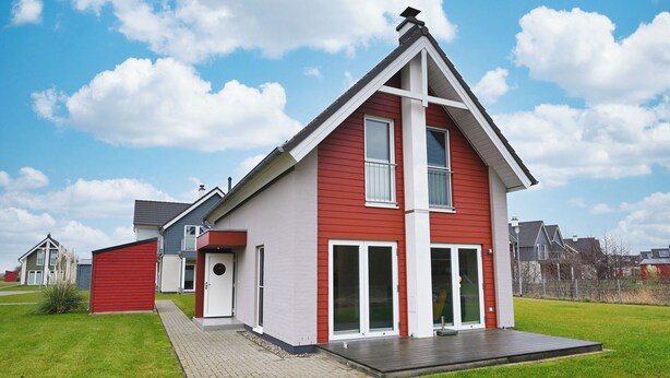 A modern two-story house with a red and white exterior, a front porch, and a well-maintained lawn. - Vacation home "Noordkant 17" with its own sauna (Büsum)