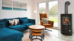 A modern living room with a blue sofa, a wooden coffee table, a striped armchair, and a black wood-burning stove. - Vacation home "Noordkant 17" with its own sauna (Büsum)
