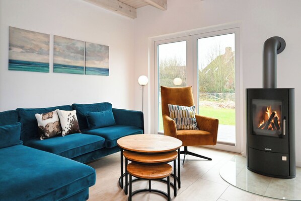 A modern living room with a blue sofa, a wooden coffee table, a striped armchair, and a black wood-burning stove. - "Noordkant 17" Vacation Home with Private Sauna (Büsum)