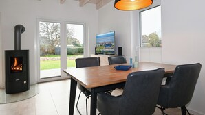 A modern dining area with a wooden table, black chairs, a black stove, and a large window with a view of the outdoors. - Vacation home "Noordkant 17" with its own sauna (Büsum)