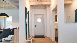 A hallway with a wooden ceiling, a white door with a circular window, a bench, and a dining area with chairs and a table. - Vacation home "Noordkant 17" with its own sauna (Büsum)