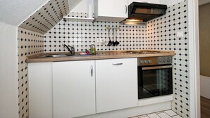 Pieni, käytännöllinen keittiö, jossa on valkoiset kaapit, liesi ja pesuallas.