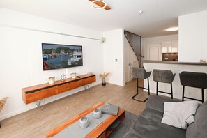 A modern living room with a wooden console table, a grey sofa, and a TV mounted on the wall. - Huus Rehders - Holiday home for 4 people in a quiet location (Büsum)