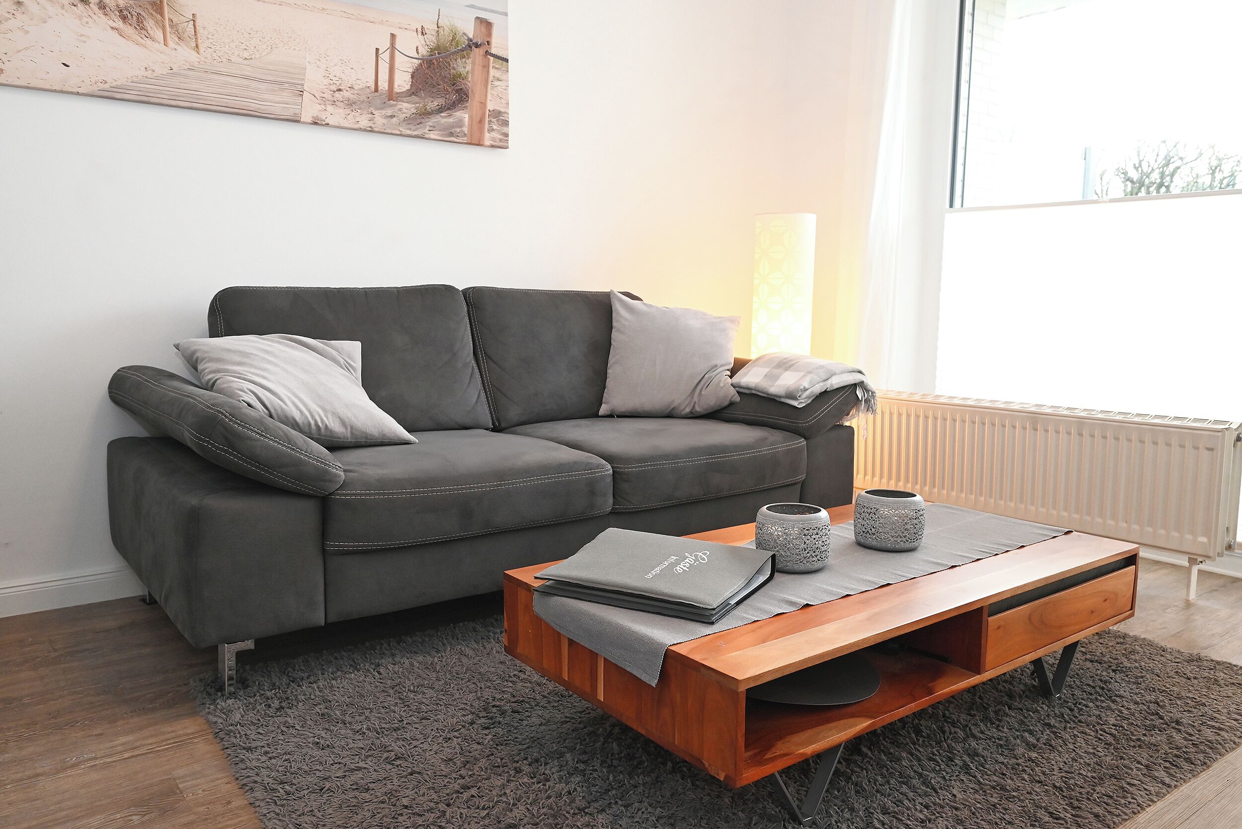 A modern living room with a grey sofa, a wooden coffee table, and a large window.