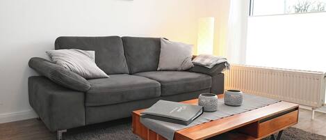 A modern living room with a grey sofa, a wooden coffee table, and a large window.