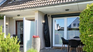 Una proprietà residenziale con patio coperto, porta scorrevole in vetro, un piccolo spazio esterno con sedie e un giardino con diverse piante.