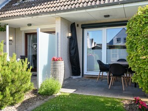 A residential property with a covered patio, a sliding glass door, a small outdoor seating area with chairs, and a garden with various plants. - Huus Rehders - Holiday home for 4 people in a quiet location (Büsum)