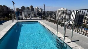 Ein rechteckiger Pool mit klarem, blauem Wasser, umgeben von einem Metallzaun und Betonstufen.