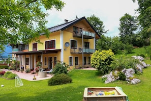 A two-story house with a balcony, surrounded by a well-maintained garden and a view of the countryside. - Vacation apartment for up to 5 people with covered terrace and garden (Schönau am Königssee)