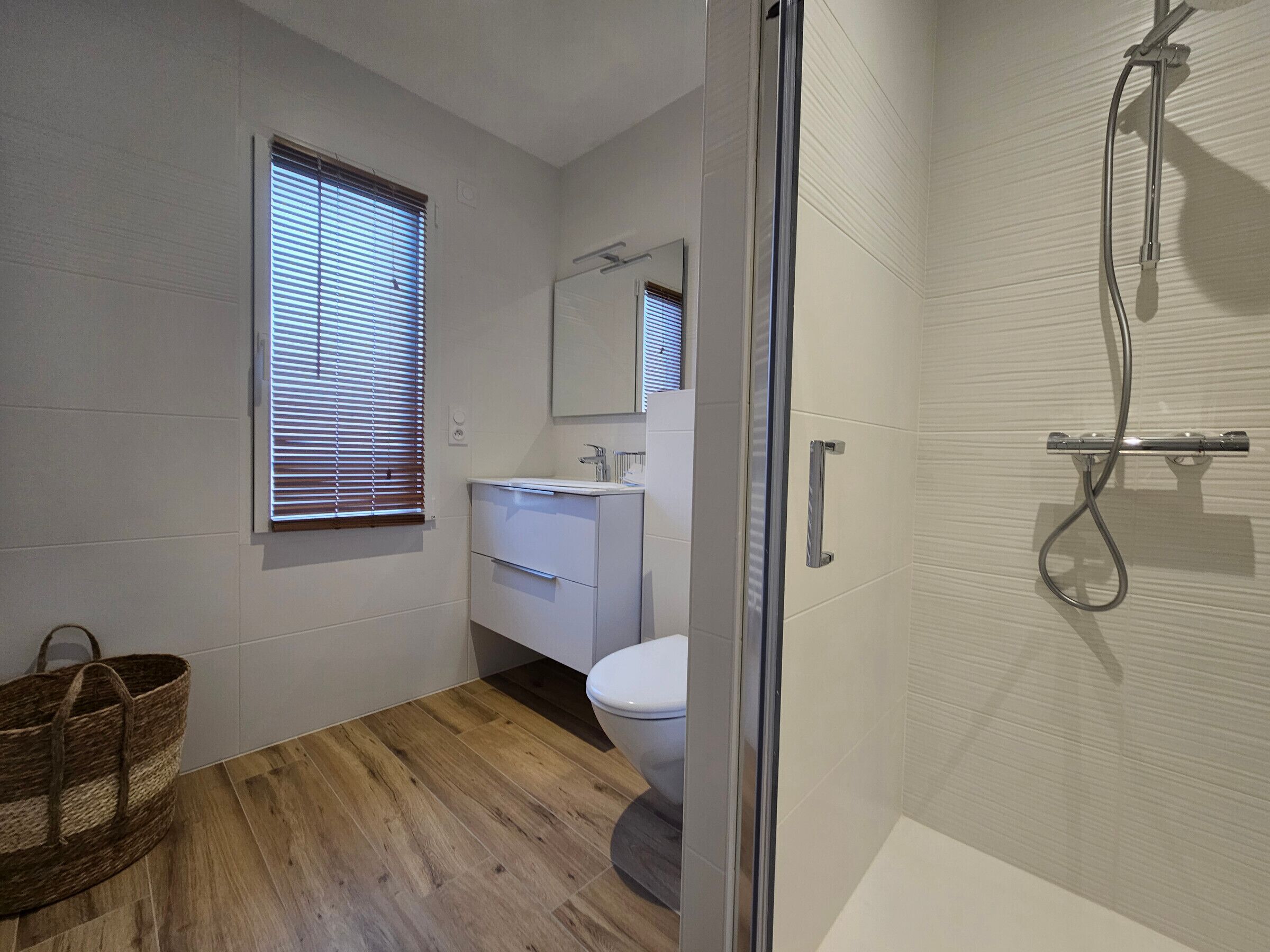 A bathroom with a wooden floor, a white sink, a toilet, and a shower.