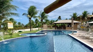 A swimming pool with a circular section, surrounded by palm trees and lounge chairs. - Beachfront Paradise in Condo w/ Pool in Itacimirim - Rsvs (Camaçari)