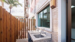 A narrow outdoor area with a wooden fence, a small sink, and a window with a view of a building in the background. - Beachfront Paradise in Condo w/ Pool in Itacimirim - Rsvs (Camaçari)