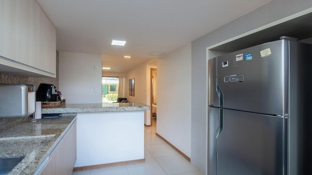 A modern kitchen with a central island, stainless steel appliances, and a view to the outside. - Beachfront Paradise in Condo w/ Pool in Itacimirim - Rsvs (Camaçari)
