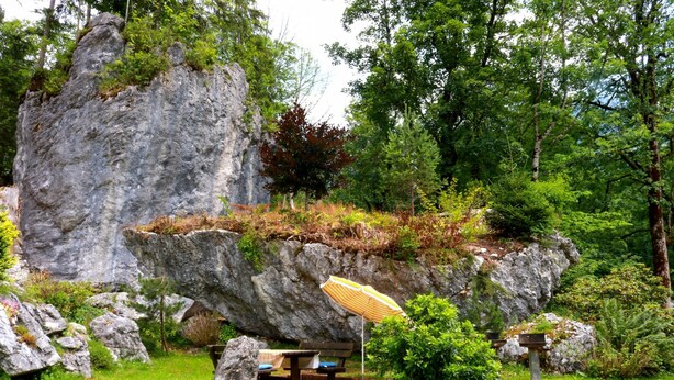 Um jardim com uma formação rochosa, mesa de piquenique e guarda-sol.