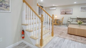 A staircase with wooden balusters, a dining area with a table and chairs, a sofa, and a coffee table with a vase of flowers. - Walk to Sagamore Beach! Curated + Spacious Cottage (Sagamore Beach)
