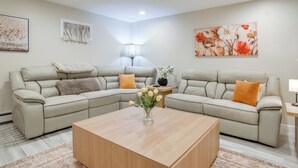 A modern living room with a sectional sofa, a wooden coffee table, and a vase of flowers. - Walk to Sagamore Beach! Curated + Spacious Cottage (Sagamore Beach)