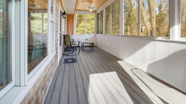 A covered porch with a wooden floor, white walls, and large windows offering a view of trees. - Walk to Sagamore Beach! Curated + Spacious Cottage (Sagamore Beach)