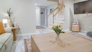 A modern living room with a wooden coffee table, a vase with flowers, a sofa, and a staircase leading to another room. - Walk to Sagamore Beach! Curated + Spacious Cottage (Sagamore Beach)