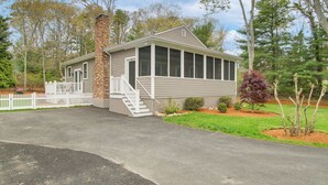 A single-story house with a brick chimney, a covered porch, and a front yard with landscaping. - Walk to Sagamore Beach! Curated + Spacious Cottage (Sagamore Beach)
