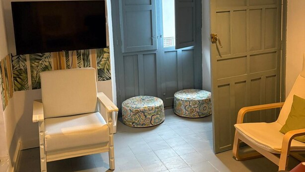 Une pièce avec un téléviseur fixé au mur, deux poufs à motifs et deux fauteuils.