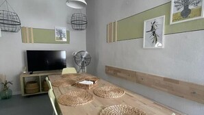 Un espace repas comprenant une longue table en bois, des sets de table en fibres tressées, un téléviseur et des œuvres d’art accrochées au mur.