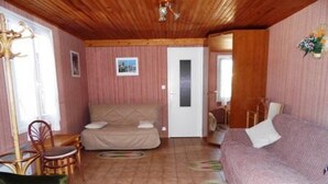 Ein gemütliches Zimmer mit einem Bett, einem grünen Sessel, einer Holzbalkendecke und einer Tür zu einem anderen Raum.