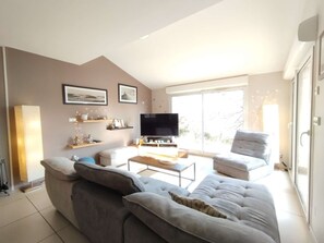 Una sala de estar moderna con un sofá, una mesa de centro y un televisor. Hay cuadros enmarcados en la pared y un ventanal que proporciona luz natural.