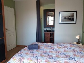 Une chambre à coucher avec un lit, une lampe de chevet, une salle de bain avec un lavabo et un tableau encadré au mur.