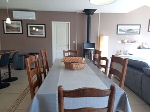 A dining area with a long table, wooden chairs, a woven basket, a fireplace, and framed pictures on the walls.