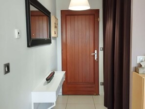 A hallway with a wooden door, a white console table with a remote control, and a wall-mounted mirror. - 4-bed house with garden near Cahors, smart TV & Wii, peaceful and comfortable (Pradines)